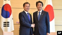 Presiden Korea Selatan Moon Jae-in (kiri) berjabat tangan dengan PM Jepang Shinzo Abe dalam pertemuan di Tokyo, 9 Mei 2018 (foto: dok). Jepang dan Korsel sedang terlibat dalam pertikaian ekonomi. 