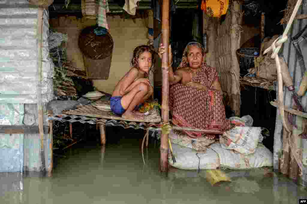 A woman and a young girl sit in their flooded house in Sunamganj, Bangladesh.
