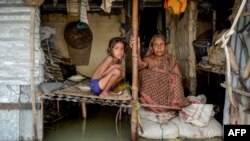 A woman and a young girl sit in their flooded house in Sunamganj, Bangladesh.
