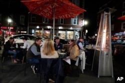 Diners have dinner outdoors, Nov. 6, 2020, in Boston's North End. More stringent coronavirus restrictions are now in effect in Massachusetts, including requiring restaurants to stop providing table service at 9:30 p.m.