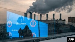 Arhiva - Pešaci i elektronski displej na kome se emituju saveti za prevenciju širenja Kovida 19, dok se u pozadini diže dim iz fabrike, u Moskvi, 3. decembra 2020.