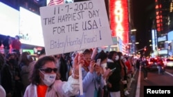 Seorang perempuan mengacungkan poster dan lainnya merayakan pemberitaan media bahwa calon presiden dari Partai Demokrat, Joe Biden, memenangi pemilihan presiden AS 2020, di Times Square, New York City, Sabtu, 7 November 2020. (Foto: Reuters)