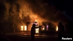 Para pria berdiri di depan toko yang terbakar akibat serangan roket dalam konflik militer Armenia dan Azerbaijan terkait kawasan separatis, Nagorno-Karabakh, di Stepanakert, 3 Oktober 2020. (Foto: Reuters)