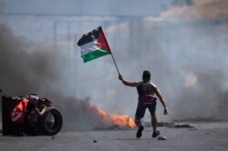 A protester waves the Palestinian flag during clashes with the Israeli forces at the Hawara checkpoint, south of the West Bank city of Nablus, May 14, 2021.