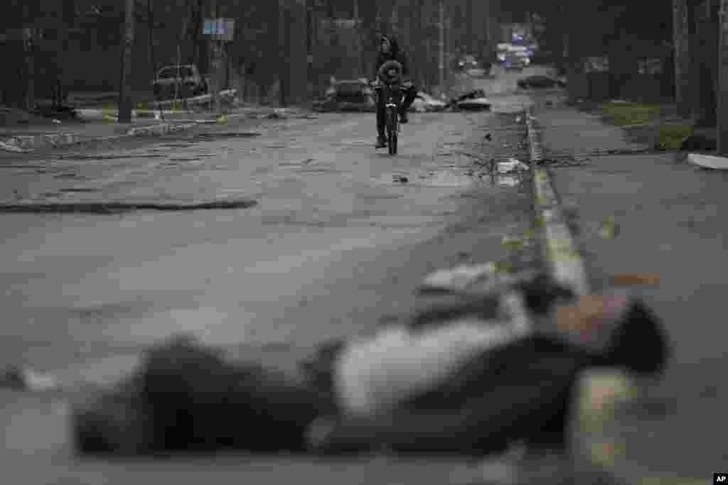 Un hombre y un niño pasan en bicicleta junto a cadáveres de civiles que yacen en la calle del suburbio de Bucha, en Kiev, tras la ocupación rusa, en Ucrania, el 2 de abril de 2022.