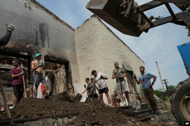 Young volunteers clear debris from a building destroyed by a Russian rocket while enjoying a techno performance by a DJ in the village of Yahidne, Chernihiv Region, Ukraine, Sunday, July 24, 2022.