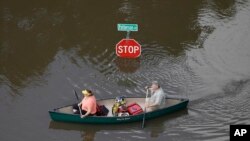 People canoe through floodwaters past a stop sign near Bear Creek Park in Houston, May 30, 2015.