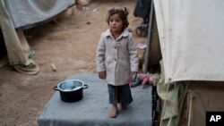 A child waits for her mother as she stands outside the family tent home at Ritsona refugee camp near Athens. About 600 people, mostly families with small children, live in tents in the camp. (AP Photo/Petros Giannakouris)