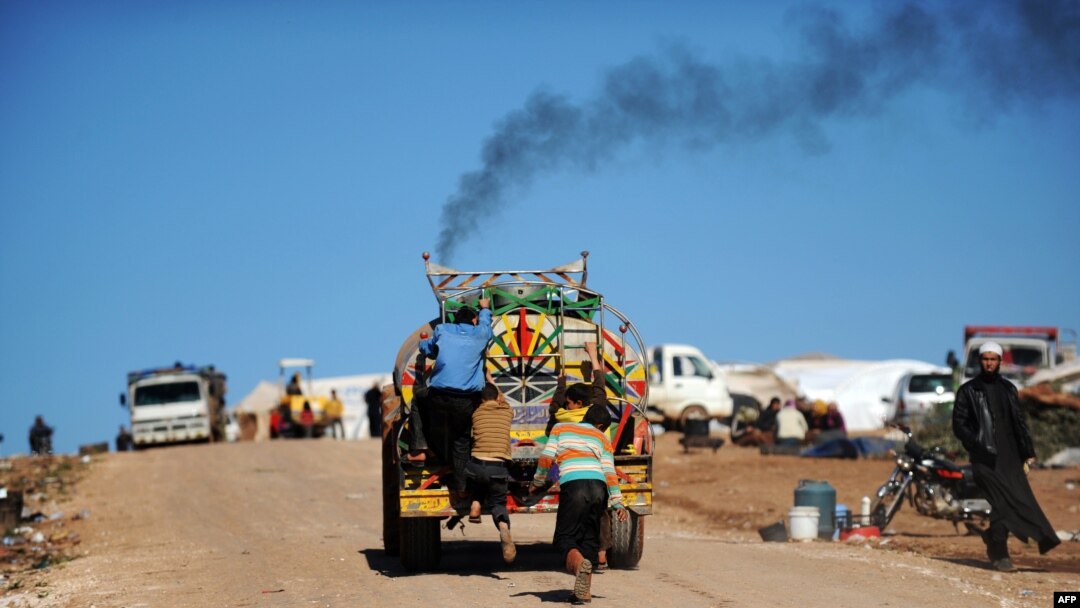 FILE - Syrian internally displaced children jump on the back of a truck at the Atme refugee camp, along the Turkish border in the northwestern Syrian province of Idlib. 