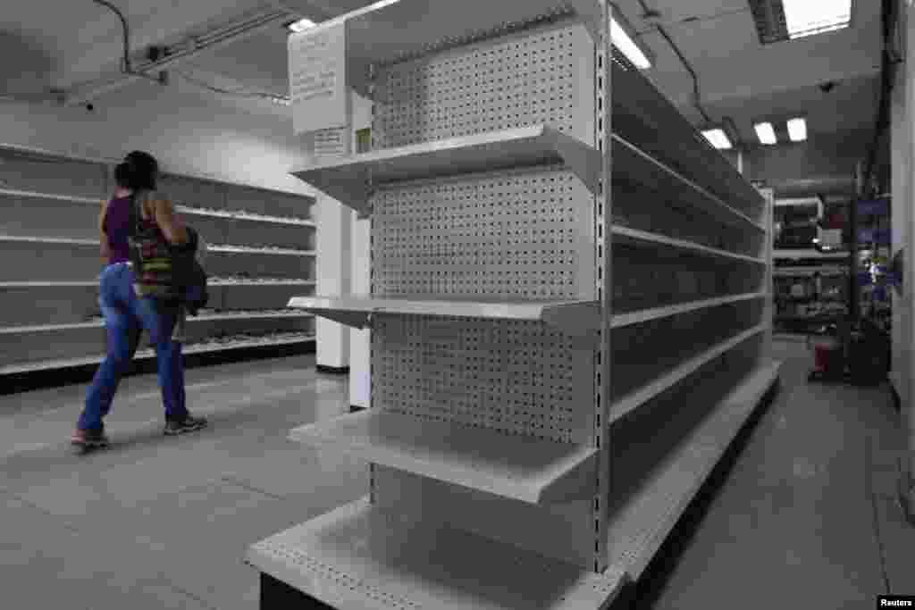 A woman walks past empty shelves at a drugstore in Caracas, Venezuela.