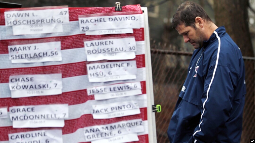 Un hombre apesadumbrado frente a una bandera cubierta con los nombres de las víctimas de Newtown.