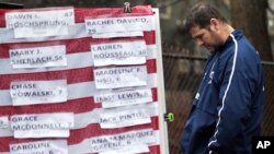 Un hombre apesadumbrado frente a una bandera cubierta con los nombres de las víctimas de Newtown.