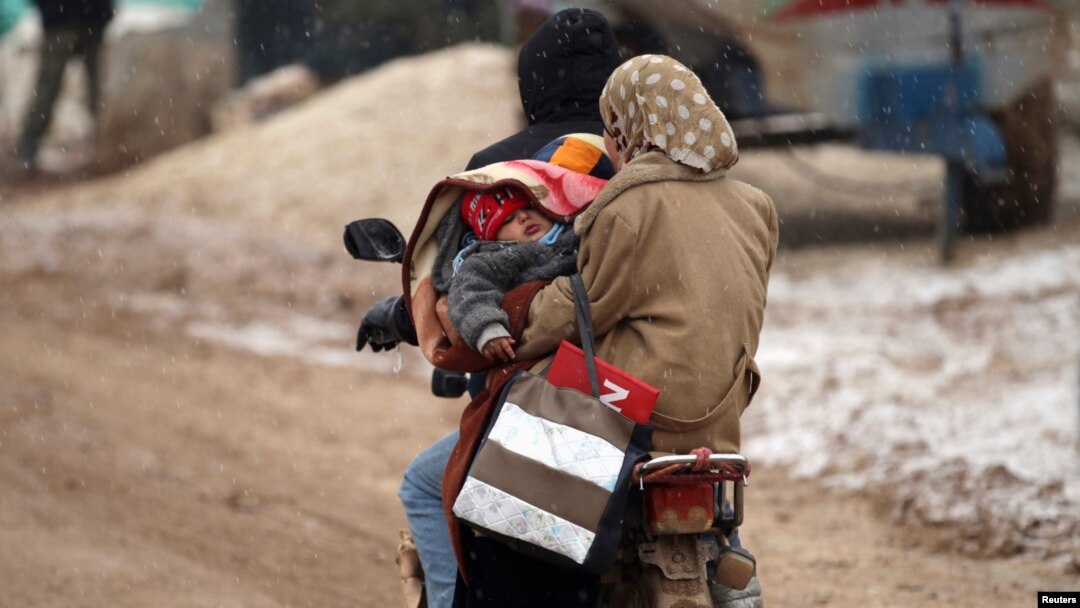 FILE - Internally displaced refugees carry a baby on a motorcycle during a snow storm inside Salkeen refugee camp, Northern Idlib countryside, Jan. 10, 2015. 