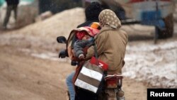 FILE - Internally displaced refugees carry a baby on a motorcycle during a snow storm inside Salkeen refugee camp, Northern Idlib countryside, Jan. 10, 2015. 