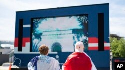 Fans watch the opening ceremony of the Tokyo 2020 Olympic Games on a big screen at the Team GB Tokyo 2020 Olympics fanzone, at Westfield, London, Friday July 23, 2021, which will be open for the next 17 days. (Dominic Lipinski/PA via AP)