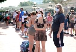 FILE - Guests wearing protective masks wait outside the Magic Kingdom theme park at Walt Disney World on the first day of reopening, in Orlando, Florida, on July 11, 2020.