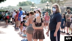FILE - Guests wearing protective masks wait outside the Magic Kingdom theme park at Walt Disney World on the first day of reopening, in Orlando, Florida, on July 11, 2020. 