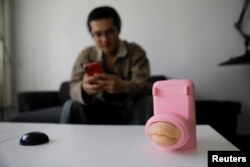 Jing Zhiyuan uses his phone near a remote kissing device, as he demonstrates how to use it during an interview with Reuters, at his home in Beijing