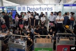Airport security personnel stand guard as travelers walk past protesters holding a sit-in rally at the departure gate of the Hong Kong International Airport in Hong Kong, Aug. 13, 2019.