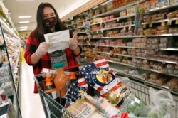 Alexandra Lopez-Djurovic checks her shopping list as she shops for a client in an Acme supermarket, in Bronxville, N.Y., July 1, 2020.