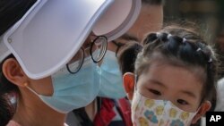 FILE - A woman and a child wearing face masks to protect against the new coronavirus visit a shopping mall in Beijing, Aug. 2, 2020.