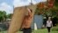 Un vecino carga un tablón de madera para cubrir las ventanas de su casa en preparación para el huracán Beryl, en Bridgetown, Barbados, el 30 de junio de 2024.