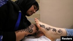 Seorang perempuan menggambar dengan inai di kaki seorang pelanggan di salon kecantikannya di Basra, Irak, 10 Maret 2019. 