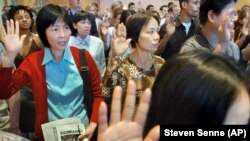 In this file photo, Mei Yu, left, and Kathy Mei, front right, both originally from China, take the oath of American citizenship in Boston, June 16, 2004. 
