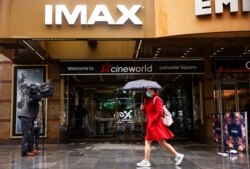 A woman holds an umbrella as she walks past a Cineworld in Leicester's Square in London, Oct. 4, 2020.