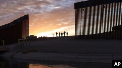 Un par de familias migrantes atraviesan una brecha en el muro fronterizo para llegar a Estados Unidos después de cruzar de México a Yuma, Arizona, para solicitar asilo, el 10 de junio de 2021.
