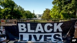 The White House is visible behind a large banner that reads Black Lives Matter that hangs on a security fence at 16th and H Street, June 8, 2020, in Washington.