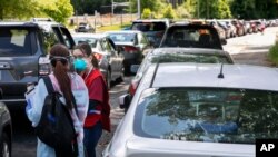 Voluntarios en Annandale, Virginia, se colocan entre cientos de automóviles para registrar a las personas que se alinean para las pruebas de COVID-19, el sábado 23 de mayo de 2020. 