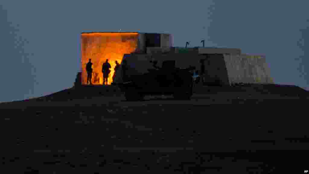 Turkish soldiers stand by a fire on a hilltop overlooking the Syrian city of Kobani, on the outskirts of Suruc, near the Turkey-Syria border, Nov. 2, 2014. 