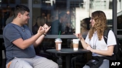 Mahasiswi jurusan penerjemah bahasa isyarat, Nikolas Carapellatti (kiri) berbincang dengan mahasiswi tuna rungu Rebeca Witzofsky di luar kafe Starbucks yang pertama menyediakan layanan bahasa isyarat, di Washington DC, 23 Oktober 2018.