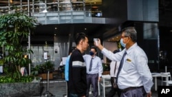 A man checks a visitor's temperature before he enters the Asia Square Tower in Singapore, March 16, 2020.