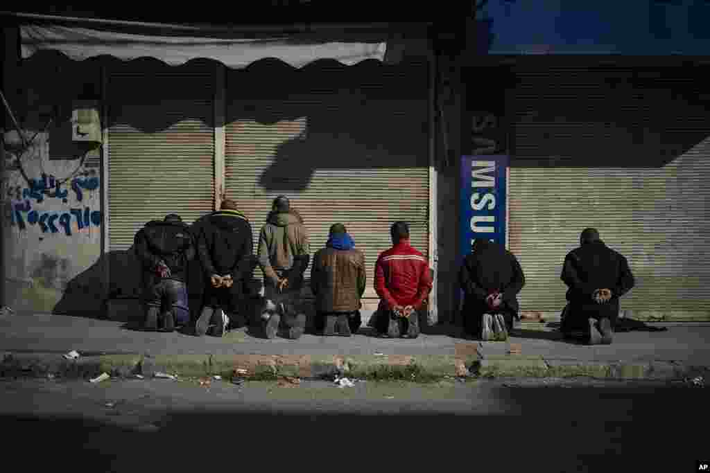 Men kneel down on the sidewalk as members of the new security forces take part in an operation to detain people suspected of being part of militias or loyalist soldiers of ousted president Bashar al-Assad in Homs, Syria.