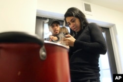 Barbara Peraza-Garcia looks at a phone while cooking in a communal kitchen while her partner, Franklin Peraza holds their daughter, Frailys, in a 'micro apartment' building in Seattle on Monday, March 11, 2024. (AP Photo/Manuel Valdes)