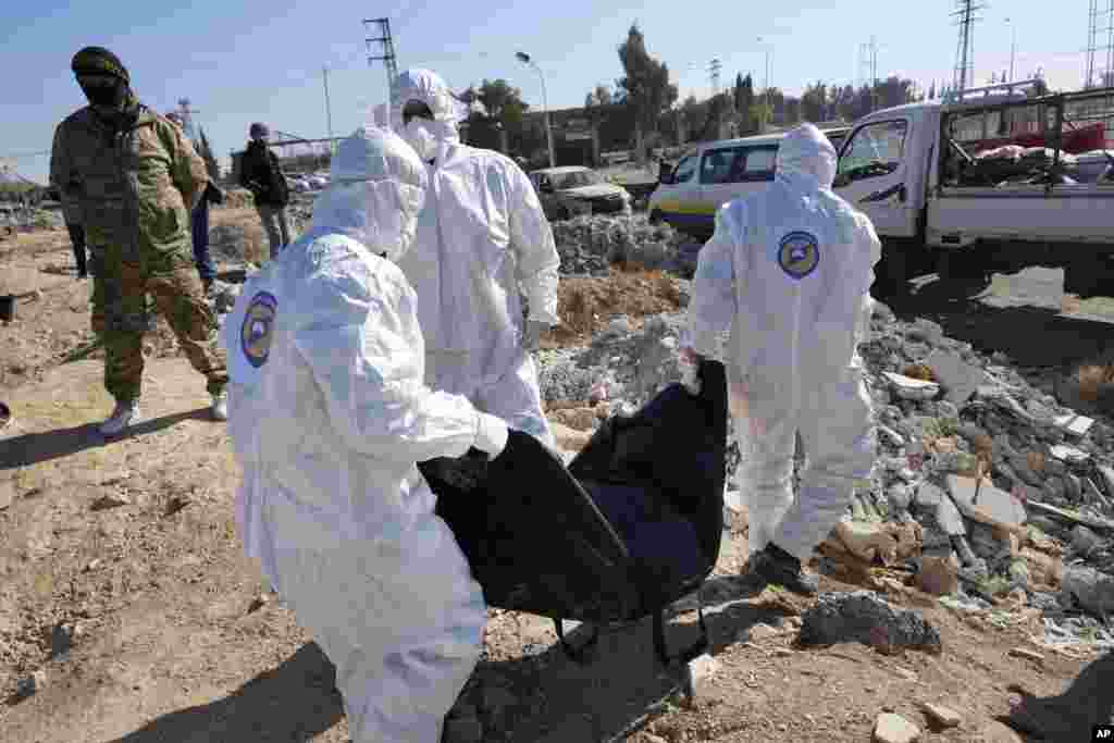 Syrian Civil Defense, known as the White Helmets, carry one of several bodies and human remains that were found at an open field on a road that links to Damascus international airport, in Damascus.