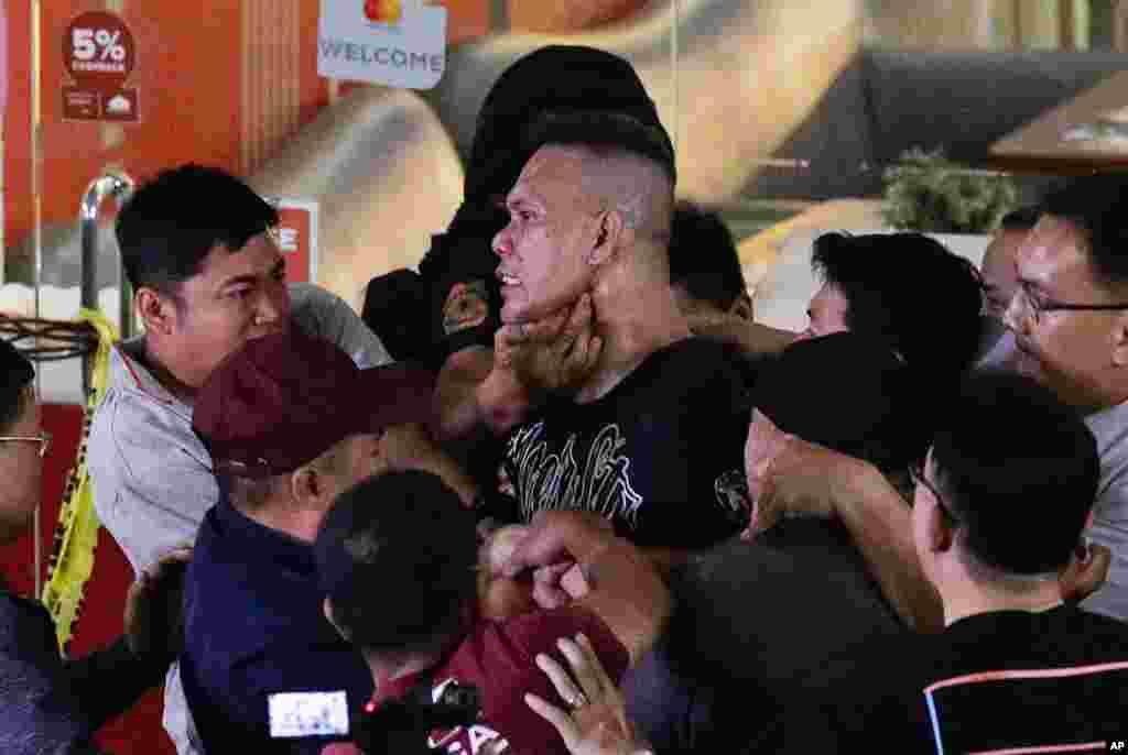 Police subdue hostage taker Archie Paray, center, as he speaks to the waiting media shortly after releasing all his hostages at the V-Mall in Manila, Philippines. 
