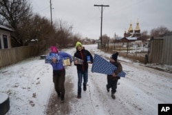 From left, Masha, 12, Tymofiy, 12, and Illia, 6, carry presents to their homes after celebrations of St. Nicholas Day in Izium, Ukraine, Dec. 6, 2024.