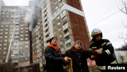 Firefighters help a woman from a building damaged during a Russian missile strike, amid Russia's attack on Ukraine, in Kyiv, Feb. 7, 2024.