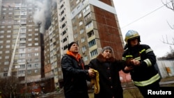Firefighters help a woman from a building damaged during a Russian missile strike in Kyiv, Ukraine, Feb. 7, 2024.