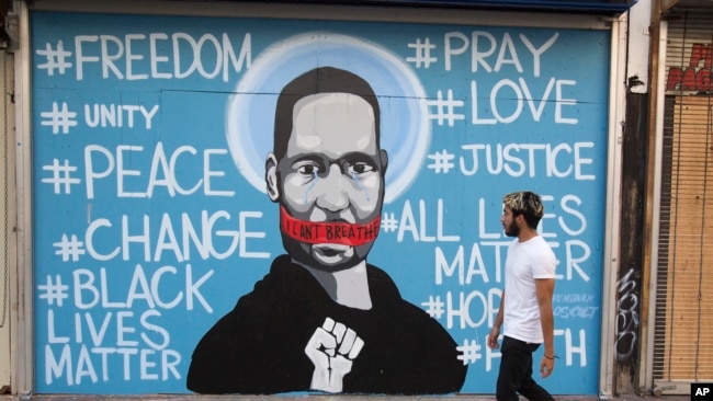 A man walks past a mural depicting George Floyd during a protest over the death of Floyd Sunday, May 31, 2020, in Los Angeles. Floyd died in Minneapolis on May 25 after he was pinned at the neck by a police officer. . (AP Photo/Ringo H.W. Chiu)