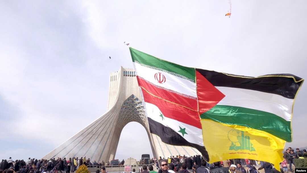 FILE - A man carries a giant banner comprising the flags of Iran, Syria, the Palestinian territories and Hezbollah, during a ceremony marking the 37th anniversary of the Islamic Revolution, in Tehran, Febr. 11, 2016. (REUTERS/Raheb Homavandi/TIMA)