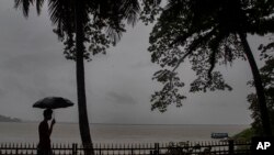An Indian man walks with his umbrella in the middle of heavy wind and rain along the river Brahmaputra in Gauhati, India, May 21, 2020. 