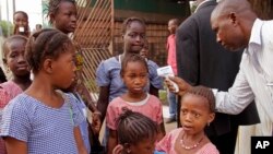 FILE - A health care worker, right, takes the temperatures of schoolchildren for signs of the Ebola virus before they enter their school in Conakry, Guinea, Jan. 19, 2015.