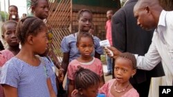 FILE - A health care worker, right, takes the temperatures of schoolchildren for signs of the Ebola virus before they enter their school in the city of Conakry, Guinea, Jan. 19, 2015.