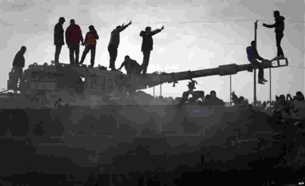 Libyan people celebrate on a tank belonging to the forces of Moammar Gadhafi in the outskirts of Benghazi, eastern Libya, Sunday, March 20, 2011. The tanks were destroyed earlier by NATO plans. (AP Photo/Anja Niedringhaus)