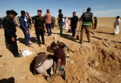 FILE - Iraqi members of the Civil Defense and Kurdish men examine an unearthed mass grave of Kurds in west of the city of Samawah, Iraq, April 14, 2019.