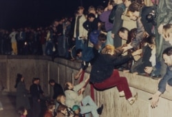 FILE - East Berliners get helping hands as they climb the Berlin Wall, Nov. 10, 1989.